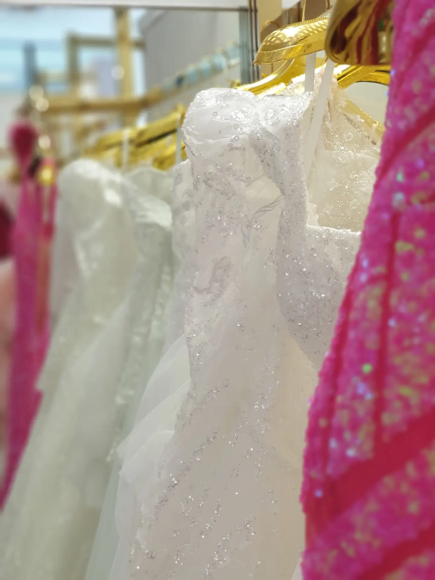White glittering wedding dress and pink sequin gown on gold hangers