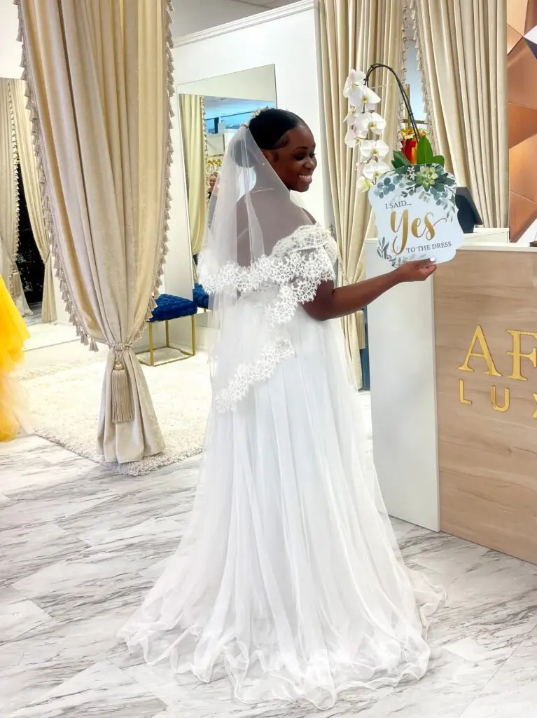 bride in an off-the-shoulder lace wedding dress holding an I Said Yes to the Dress sign
