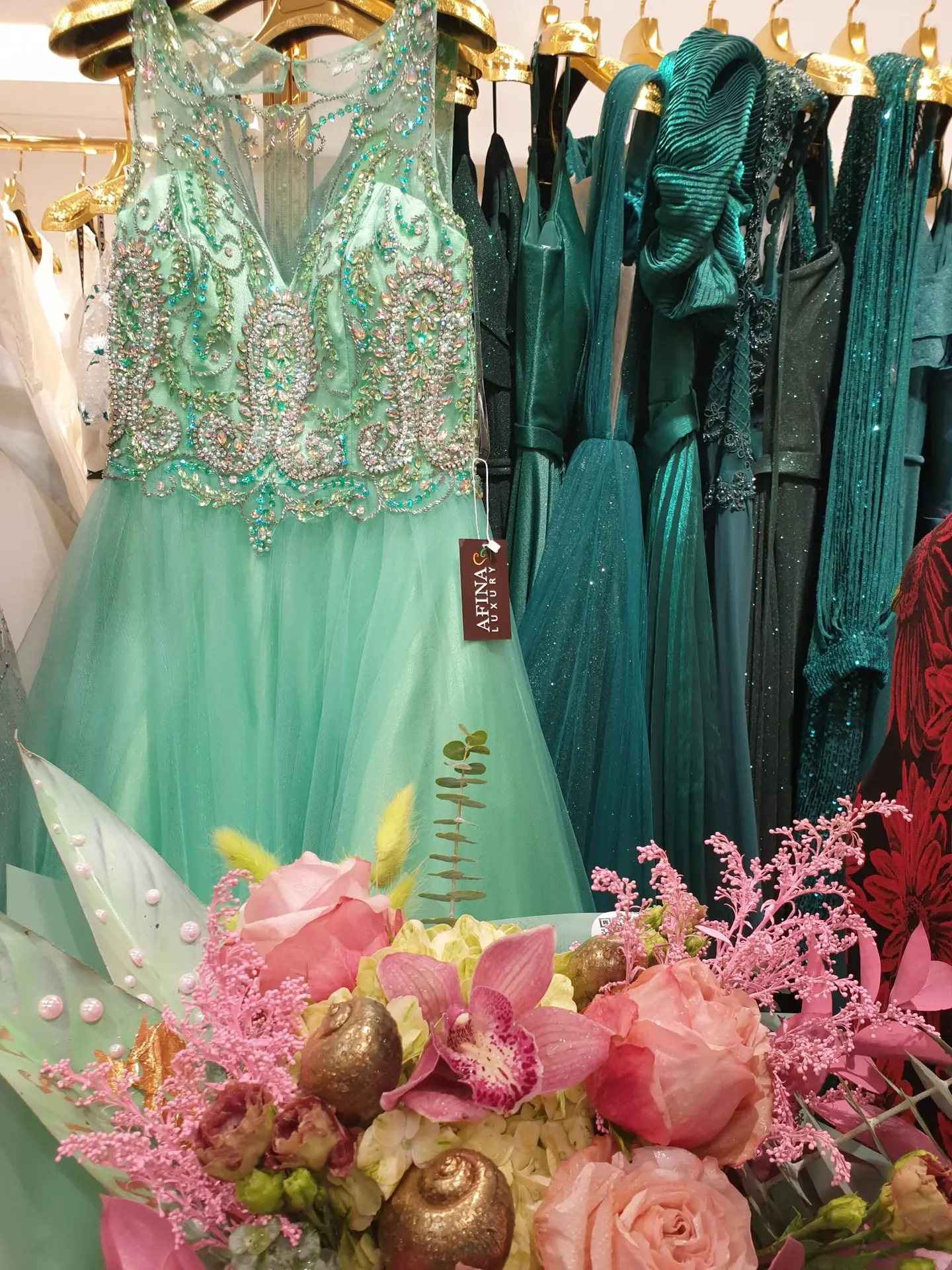 Mint green evening gown with rhinestones on a hanger next to a flower bouquet