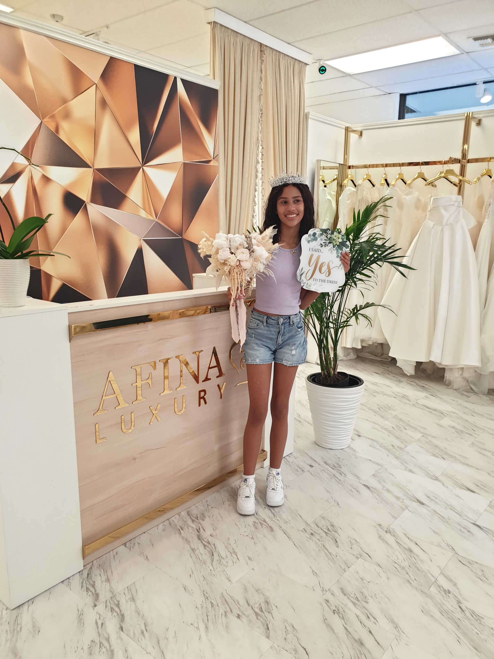 Happy customer wearing a tiara and holding an I Said Yes to the Dress sign at Afina Luxury
